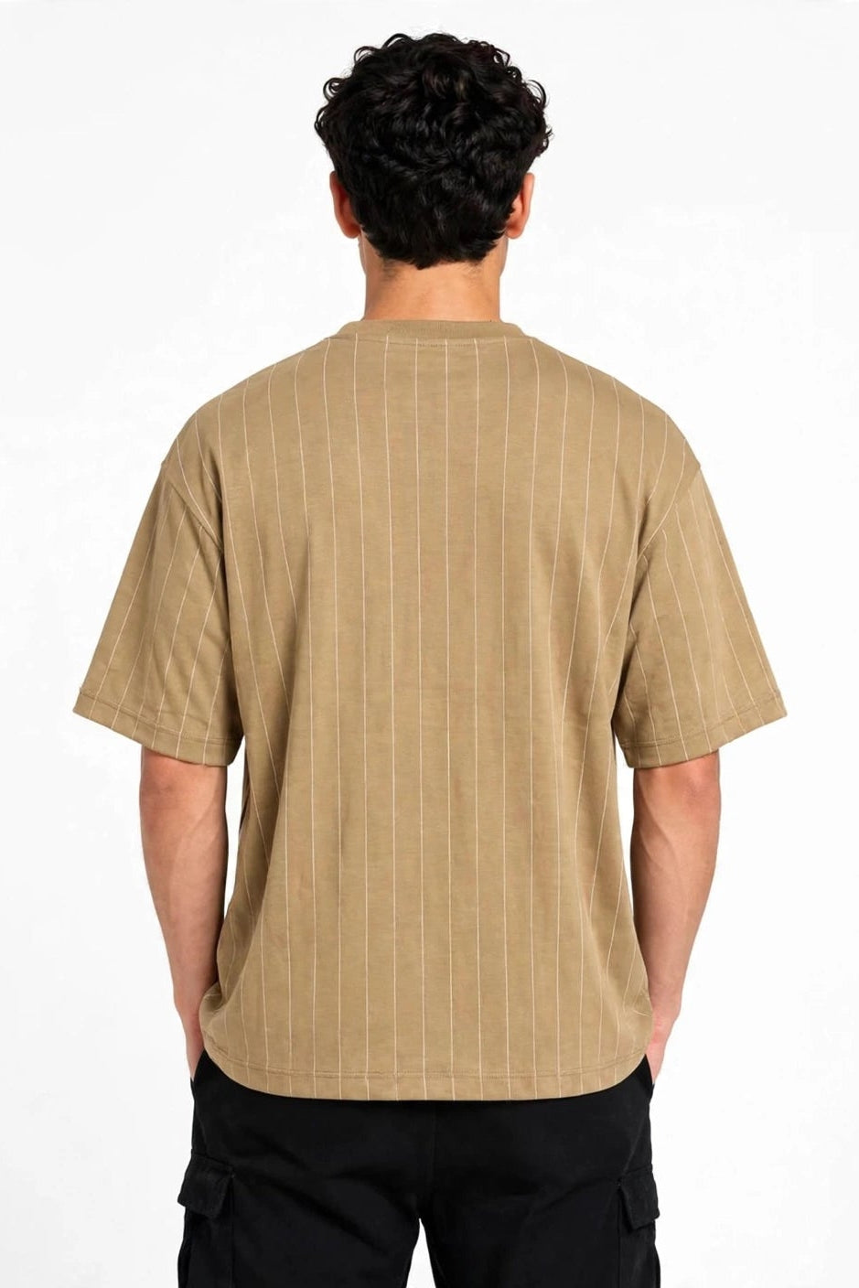 A man viewed from behind wearing a beige short-sleeve t-shirt with thin vertical pinstripes and black cargo pants, set against a plain white studio background.