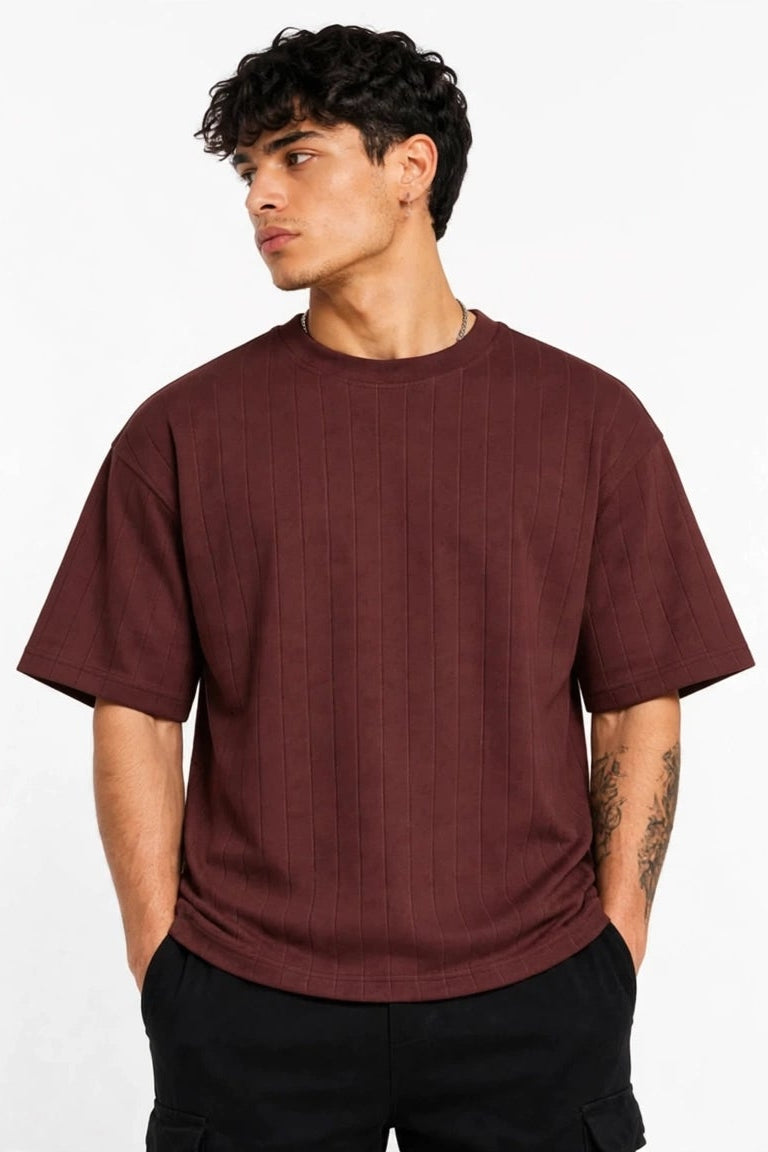 A man wearing a short-sleeve crewneck t-shirt in a dark maroon color, paired with black pants, standing against a plain white background.